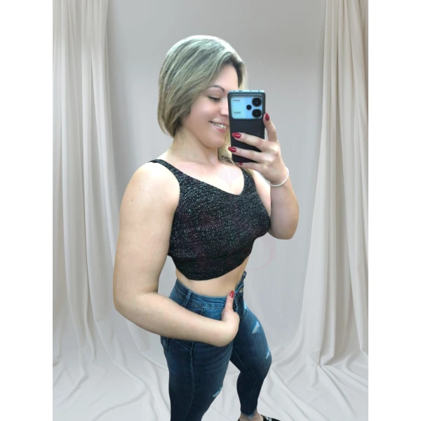 Mulher vestindo um top canelado preto, combinando com jeans rasgado, em pose casual contra fundo neutro.