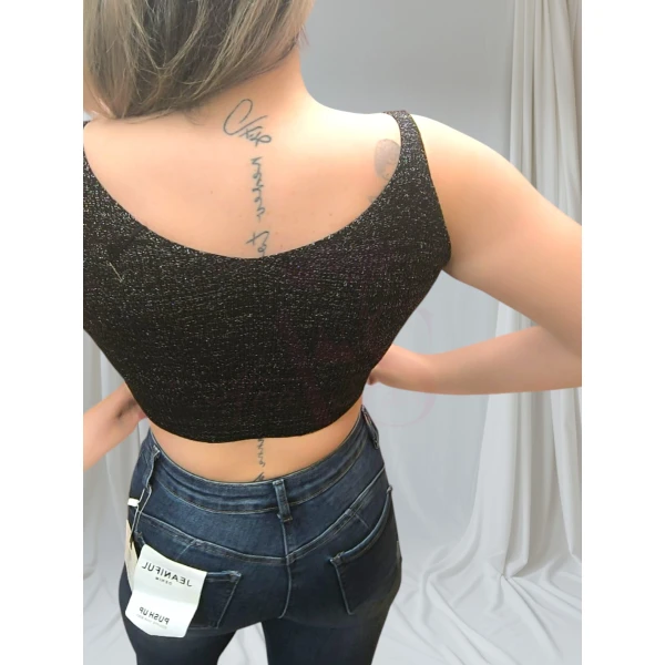 Mulher vestindo um top canelado preto, combinando com jeans rasgado, em pose casual contra fundo neutro.