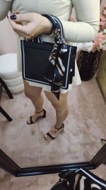 Bolsa preta feminina sofisticada com lenço decorativo e alça extra geométrica.