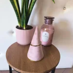 Pulseira Dourada Charme Minimalista em aço com corrente pendente sobre mesa de madeira.